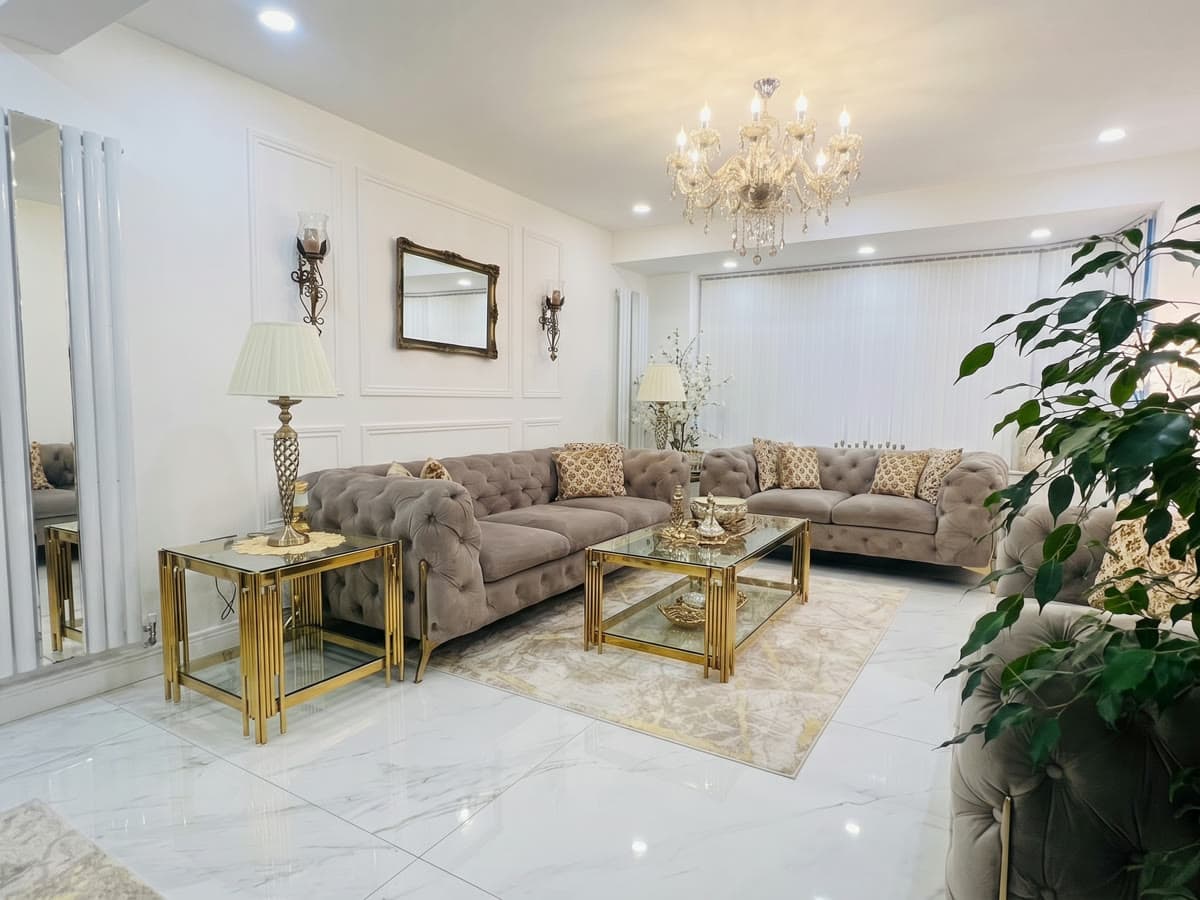 A formal living room with white panelled walls, a crystal chandelier, polished marble-effect floor tiles and grey buttoned sofas